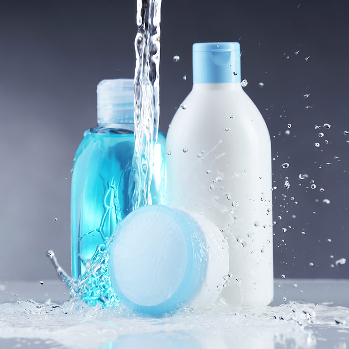 Blue and white shampoo, conditioner, and moisturizer bottles with water pouring on them