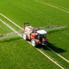 Farmer In Tractor Spraying Crops